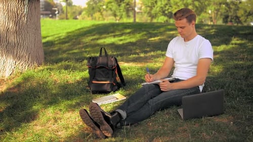 Fairhaariger Student macht Hausaufgaben im Park