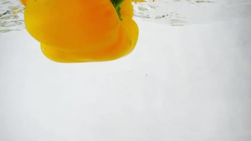 Gelbe Paprika fällt mit Spritzern und Blasen ins Wasser
