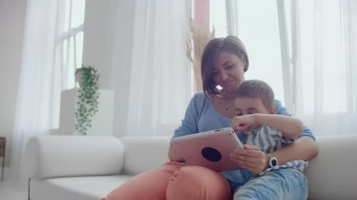 Mother and Child Using Tablet on White Sofa
