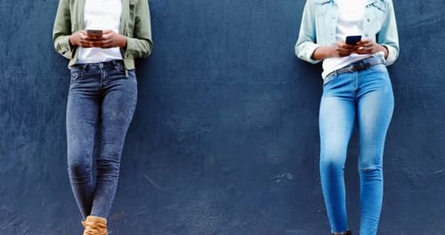 Twin sisters using mobile phone on a sidewalk in the city 4k