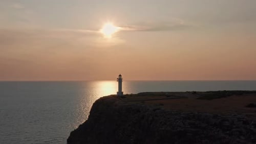 Marvelous drone flies out over silhouetted ocean cliffs and lighthouse during sunset reflecting off