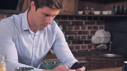 Man Uses Smartphone in Kitchen at Breakfast