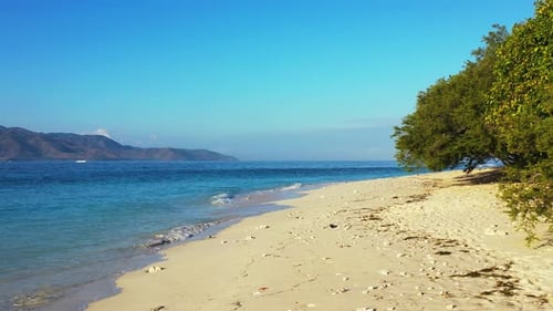 Tranquil exotic beach of tropical island with white sand washed by waves of blue sea under clear bri