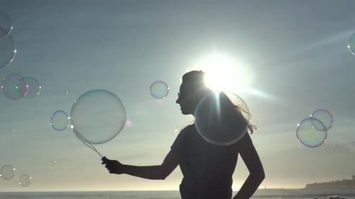 Young Adult Blowing Bubbles on a Beach at Sunset