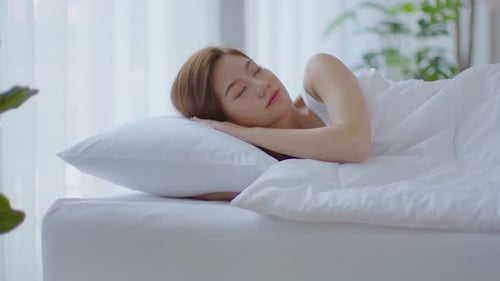 Beautiful Asian young woman close her eyes lying on bed and sleep in cozy bedroom