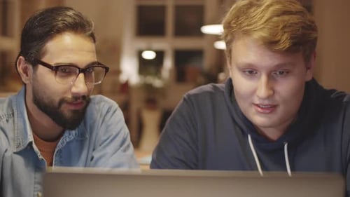 Two Young Male Coworkers Using Laptop and Talking in Office