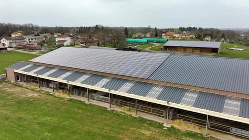 Aerial View of Blue Photovoltaic Solar Panels Mounted on Farm Building Roof for Producing Clean