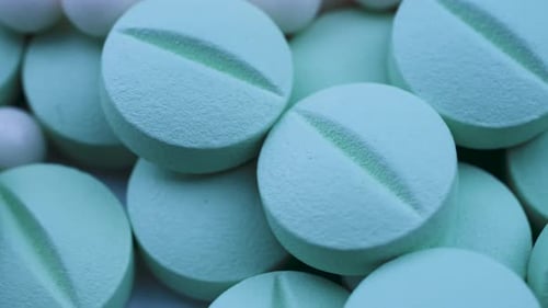 White Granules Mixed with Round Green Pills Lie on a Table and Rotate Closeup