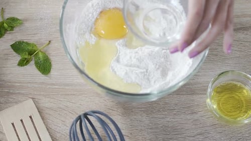 Lady adding egg to flour and mixing ingredients with wooden spoon, cake recipe