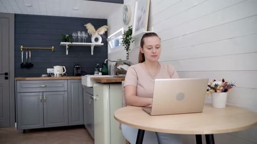 Woman Using Laptop at Kitchen Table