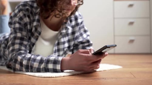 Das Schulmädchen Studen liegt mit einem Telefon in der Hand auf dem Boden. Hände halten ein Modernes
