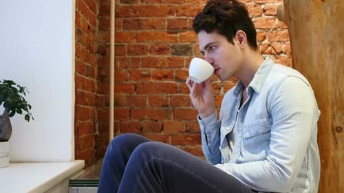 Pensive Young Man Drinking Coffee from Cup, Loft interior