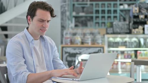 Frustrated Man Working at Laptop in Cafe
