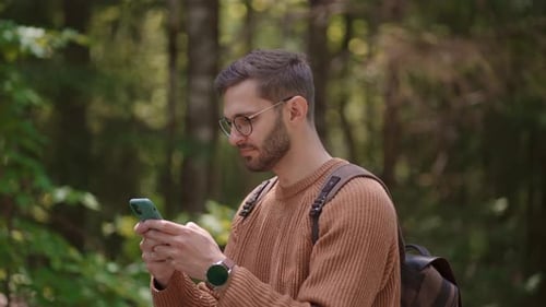 Smiling Man with Glasses with a Beard Walks Through the Woods with a Backpack and Prints a Message