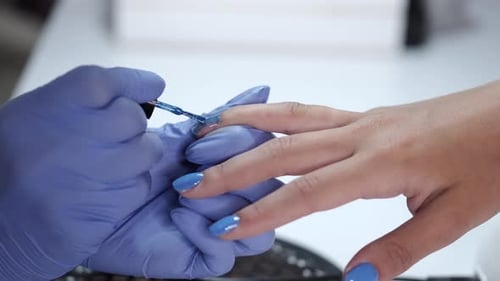 Close-up of Beautician Hands Making Blue Manicure for Client