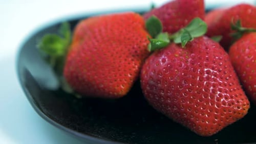 Fresh big red tasty ripe strawberries rotates slowly on a black plate on light blue background, heal