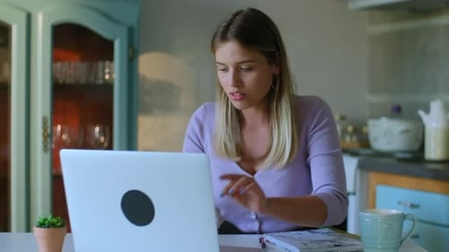 Woman Using Laptop and Writing in Notebook