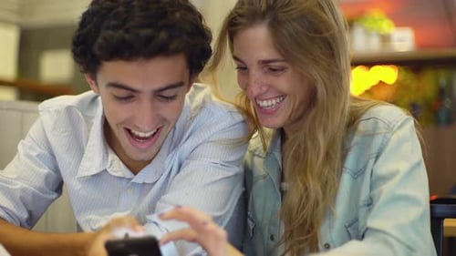 Young Man and Woman Look at Phone and Laugh