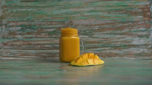 Closeup Shot of a Glass of a Mango Shake and Cut Mangoes with a Stainless Drinking Straw in It
