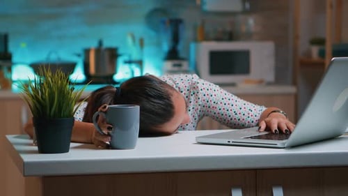 Exhausted Woman with Laptop and Mug in Kitchen
