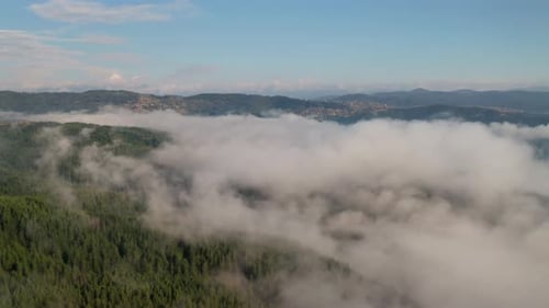 Drone flight over low clouds and morning mists covered mountain slopes