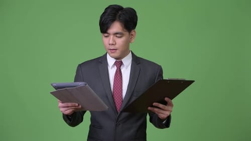 Young Adult Businessman Reading Tablet and Clipboard