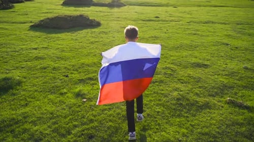 Blond Boy Runs with Flag in Green Field