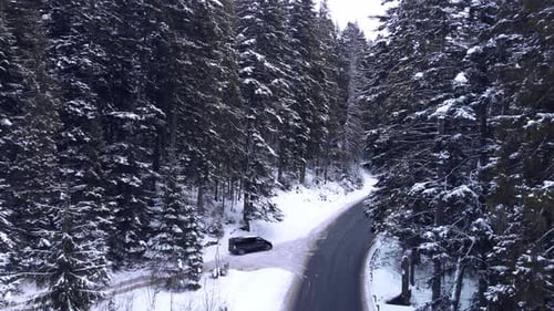 Vue aérienne de dessus des montagnes forestières enneigées avec des voitures conduisant une route d'hiver.