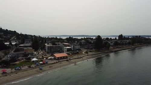 Toma de Zumbido en el sentido de las agujas del reloj que muestra a personas relajándose en Alki Beach en los suburbios Este cine 4K