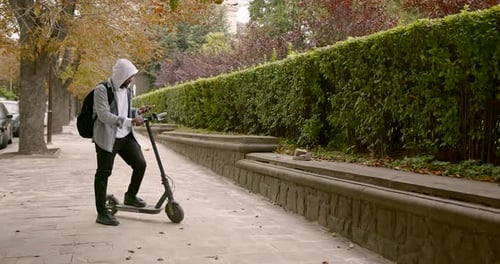 Man with Scooter and Phone on Urban Sidewalk
