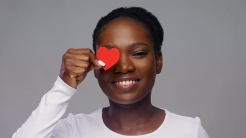 Smiling Woman Hides Eyes Behind Red Paper Hearts