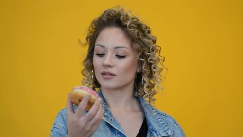 Young Woman Holds Pink Donut on Yellow Background
