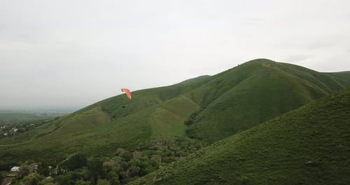 Paraglider Soaring Over Lush Green Hills