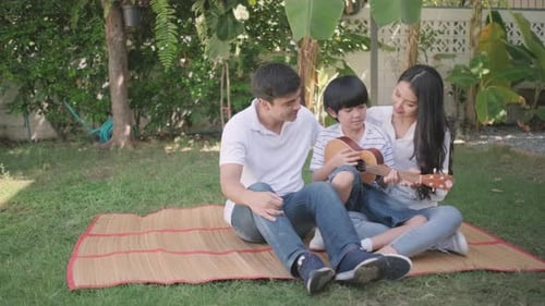 Boy play ukulele with his family mother and father in home garden with day light.