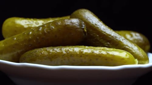 Pimply pickled cucumbers close-up on a white plate on a black background