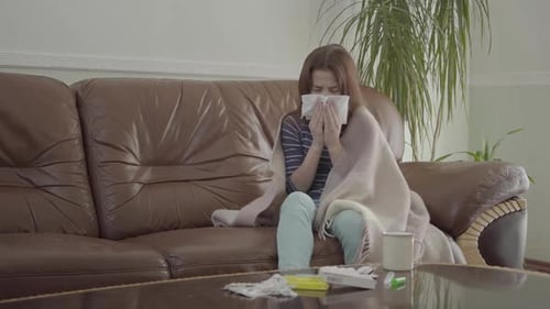 Portrait d'une adolescente enveloppée dans une couverture se mouchant dans une serviette assise sur le cuir