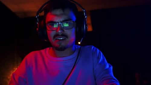 Male Gamer with Headphones Shouts Into Computer Screen After Losing an Online Game Front View