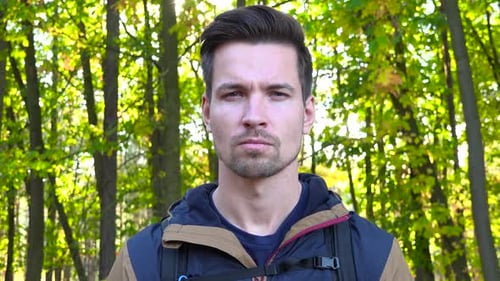 Ein junger gutaussehender Wanderer schaut an einem sonnigen Tag ernsthaft in die Kamera in einem Wald, Nahaufnahme