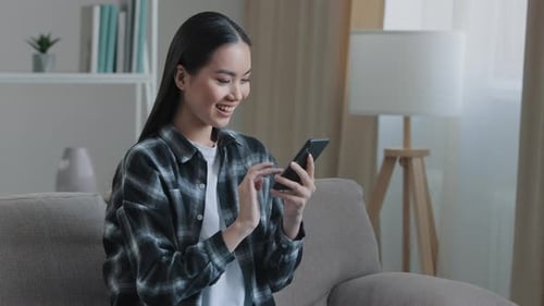 Smiling Woman Using Smartphone on Couch at Home