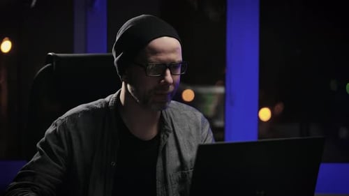 An Adult Man Works at Night on a Laptop