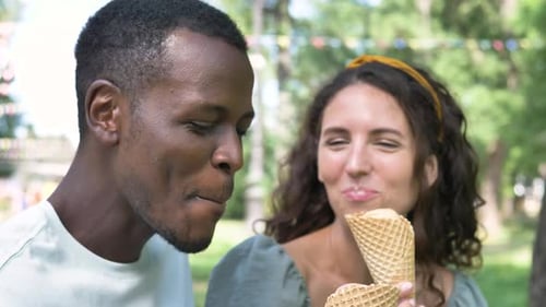 Happy Multiracial Couple Eating Illuminating Ice Cream in the Park in Summer on a Hot Day