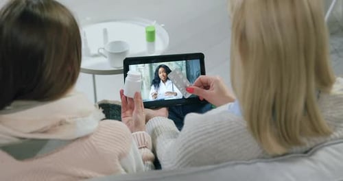 Madre e hija sentadas frente a una tableta y escuchando las instrucciones del médico