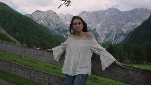 Woman Leaning on Fence in Rural Mountain Landscape