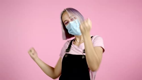 Schöne Hipsterfrau in Schutzmaske tanzt mit bunter Frisur energetisch und