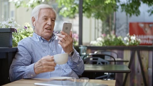 Senior Man Video Conferencing on Smartphone in Cafe