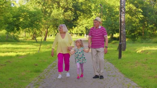 Child Girl Kid Walking with Senior Grandmother and Grandfather Family Holding Hands in Summer Park