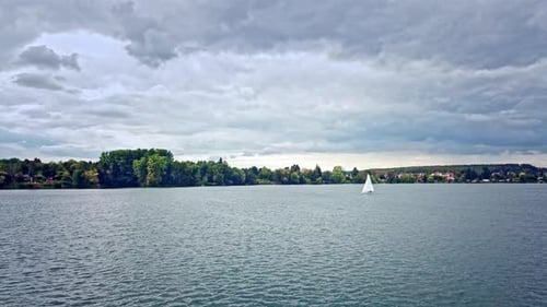 Segelboot in einem deutschen See mit Bäumen im Hintergrund und einem beeindruckenden Himmel, 4k