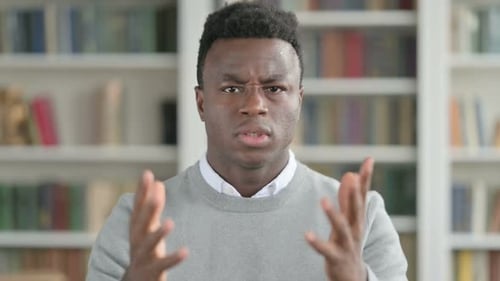 Young Adult Gesturing and Explaining in Front of Bookshelf