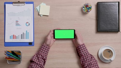 Man's Hands Over a Office Desk Holding Smart Phone with Green Screen