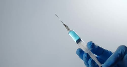 Die Krankenschwester hält eine volle Spritze mit einer langen Nadel in der Hand. Tropfen des Medikaments tropft aus der Nadel von